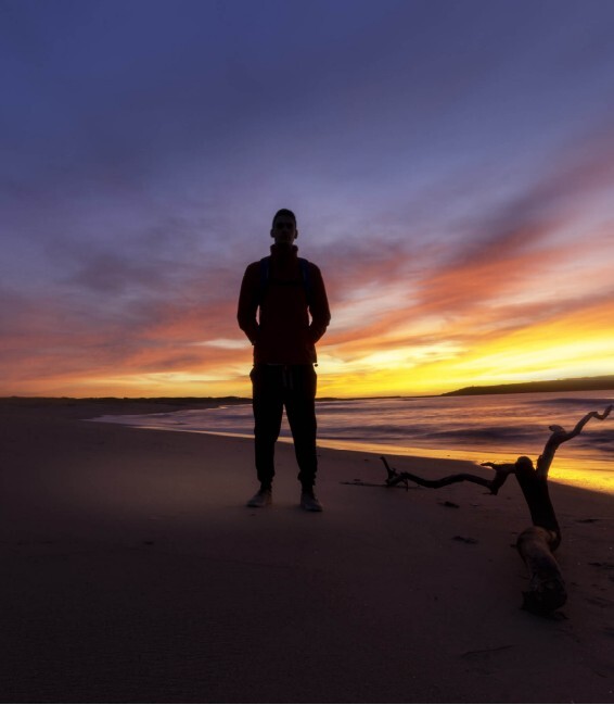 Mann steht bei Sonnenuntergang am Strand