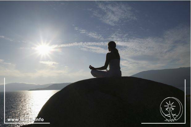 Frau meditiert auf einem Felsen am Meer