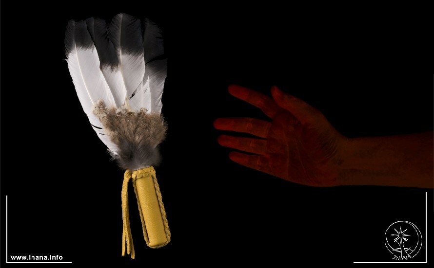 Eine Hand vor schwarzem Hintergrund greift nach einem Räucherfächer aus Federn