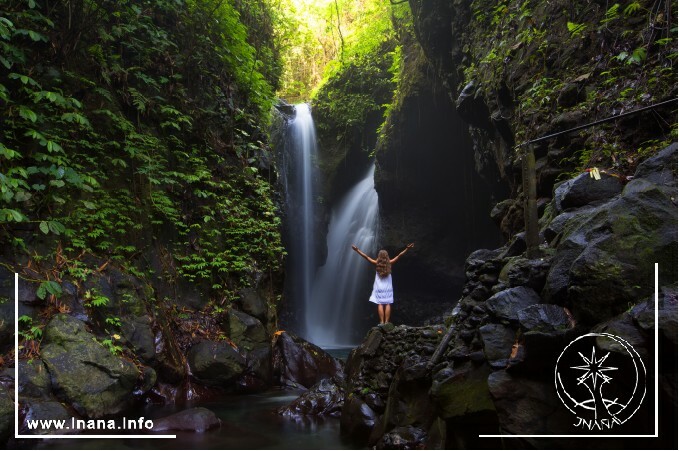 Frau mit ausgebreiteten Armen an einem Wasserfall